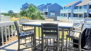 A deck with a table and chairs, overlooking a residential area with houses and a clear sky.