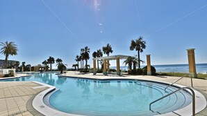 Una piscina con una estructura de sombrillas, palmeras y vistas al océano.