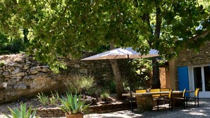 Eine Terrasse im Freien mit einer Steinmauer, einem Tisch mit Stühlen und Topfpflanzen.