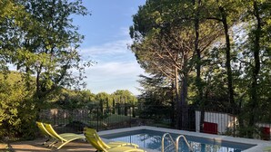 Ein Pool mit gepflastertem Deck, umgeben von Bäumen und einer Steinmauer.