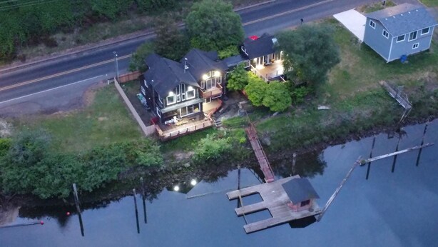 Une vue aérienne d’une maison avec une jetée qui s’avance dans un plan d’eau, le tout entouré de verdure.