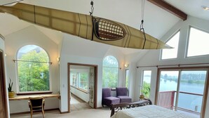 Une chambre spacieuse avec un grand lit, un bureau et une chaise. De nombreuses fenêtres offrent une vue sur l’extérieur.