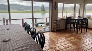 Un espace repas comprenant une table et des chaises, de grandes fenêtres donnant sur le lac et une terrasse en bois.