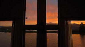 Une vue à travers une fenêtre, donnant sur un coucher de soleil au-dessus d’une étendue d’eau.