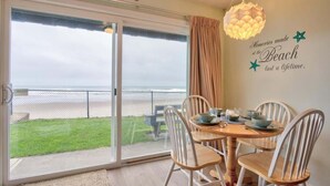 Een eetgedeelte met een tafel en stoelen, uitzicht op het strand door een schuifpui en een decoratie aan de muur met een strandthema.