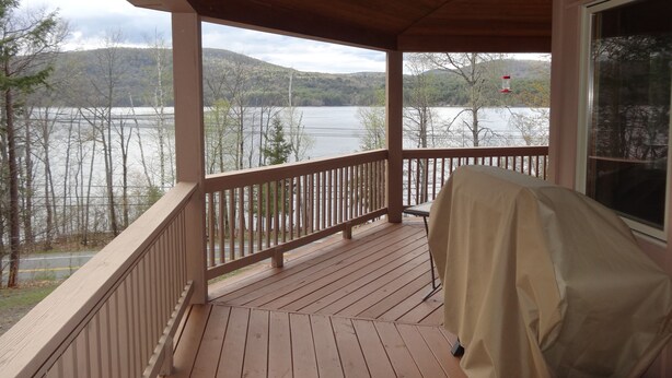 Una terraza cubierta de madera con vista a un lago y colinas.