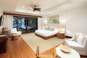Quarto de hotel moderno com cama, área de estar com uma poltrona e mesa, ventilador de teto e uma janela grande com vista.