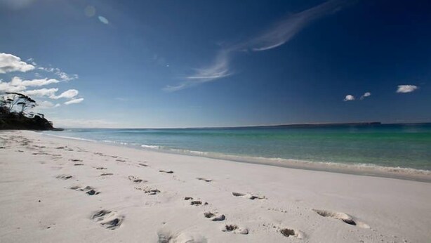 Une plage où l’on voit des empreintes de pas menant à l’eau, un ciel dégagé et une terre lointaine à l’horizon.