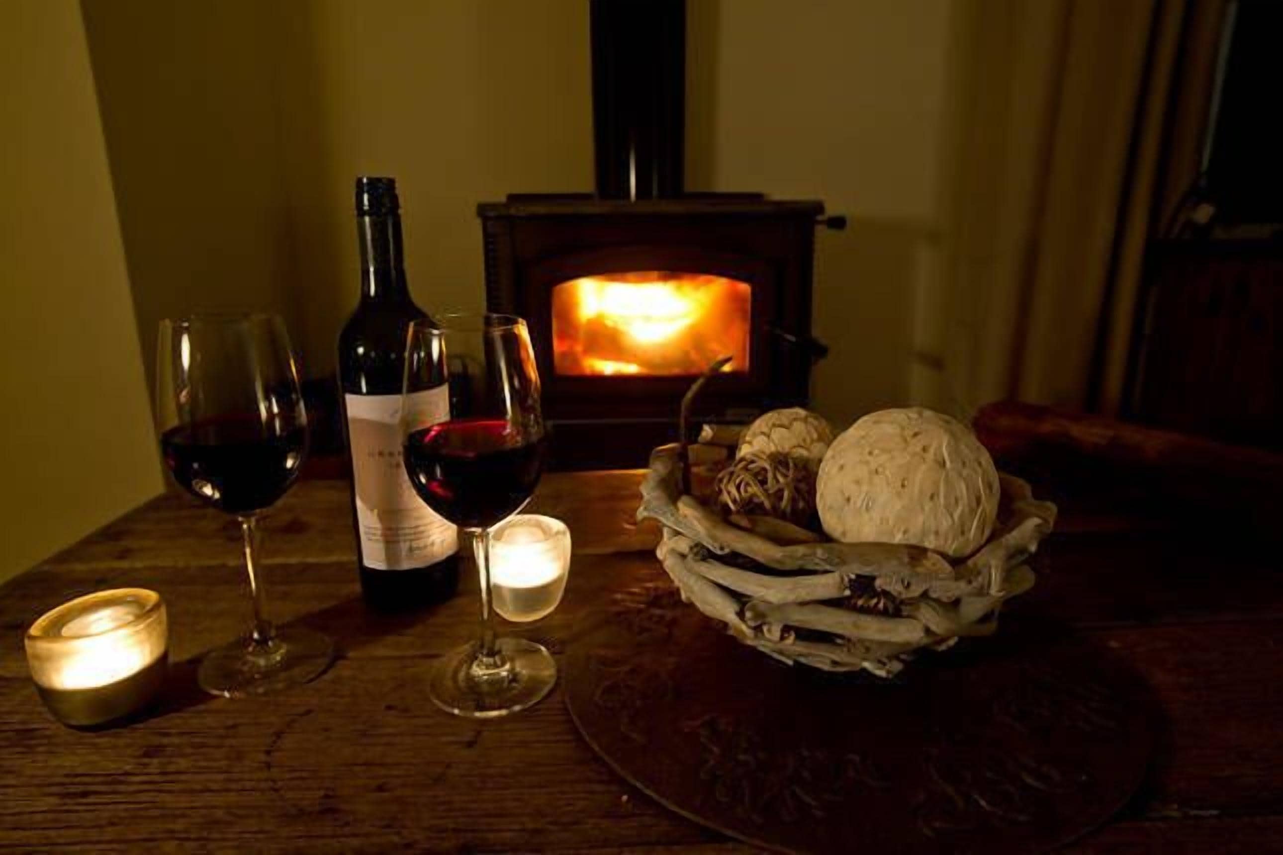 Ein Holztisch mit einer Weinflasche, zwei Weingläsern, einer Kerze und einem Brotkorb.