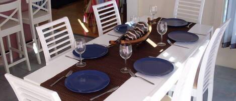 A dining table set with blue plates, white chairs, and a woven placemat.