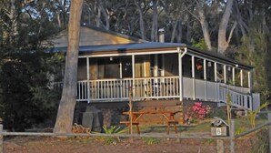 Une charmante maison de campagne située sur la côte, dotée d’un balcon, d’une terrasse en bois et d’une pancarte indiquant qu’il s’agit d’un logement de vacances.