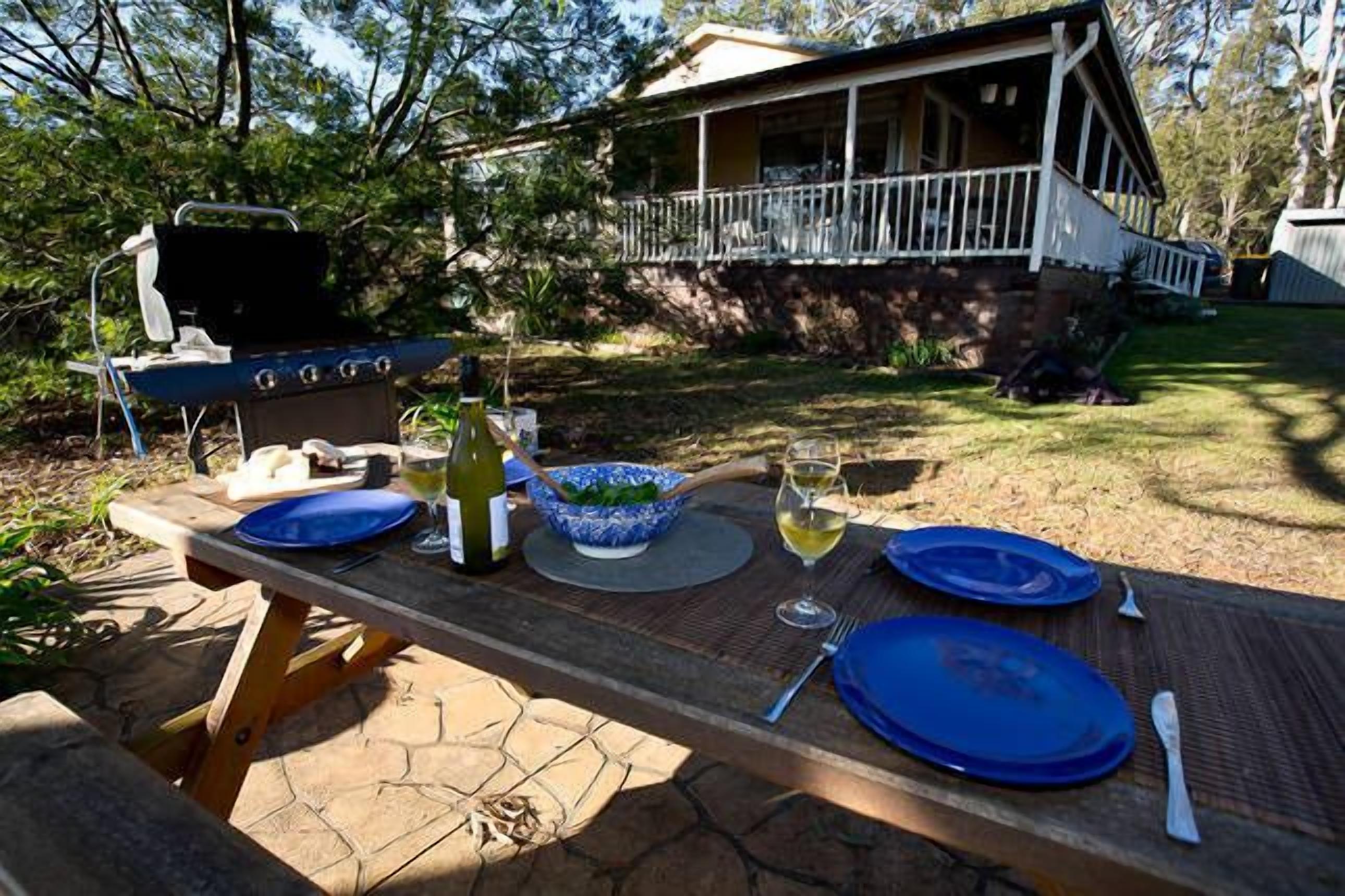 A picnic setup with a grill, blue plates, a bowl of salad, and a bottle of wine on a wooden table.