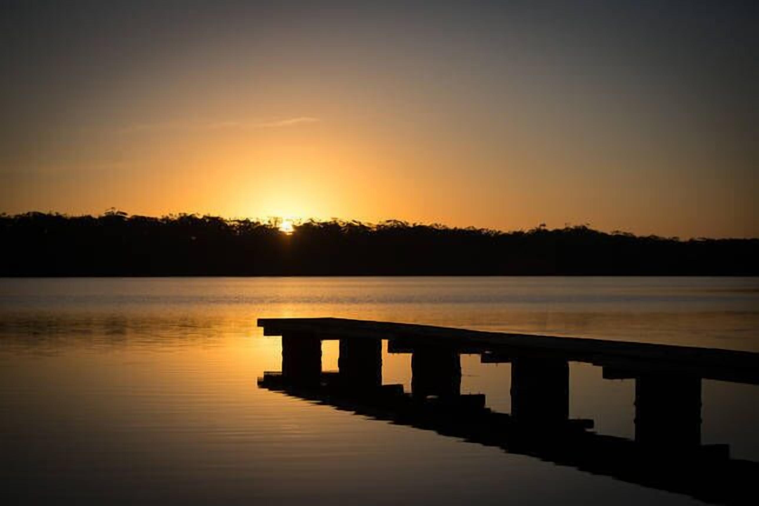 Une jetée s’avançant dans une eau calme au coucher du soleil.
