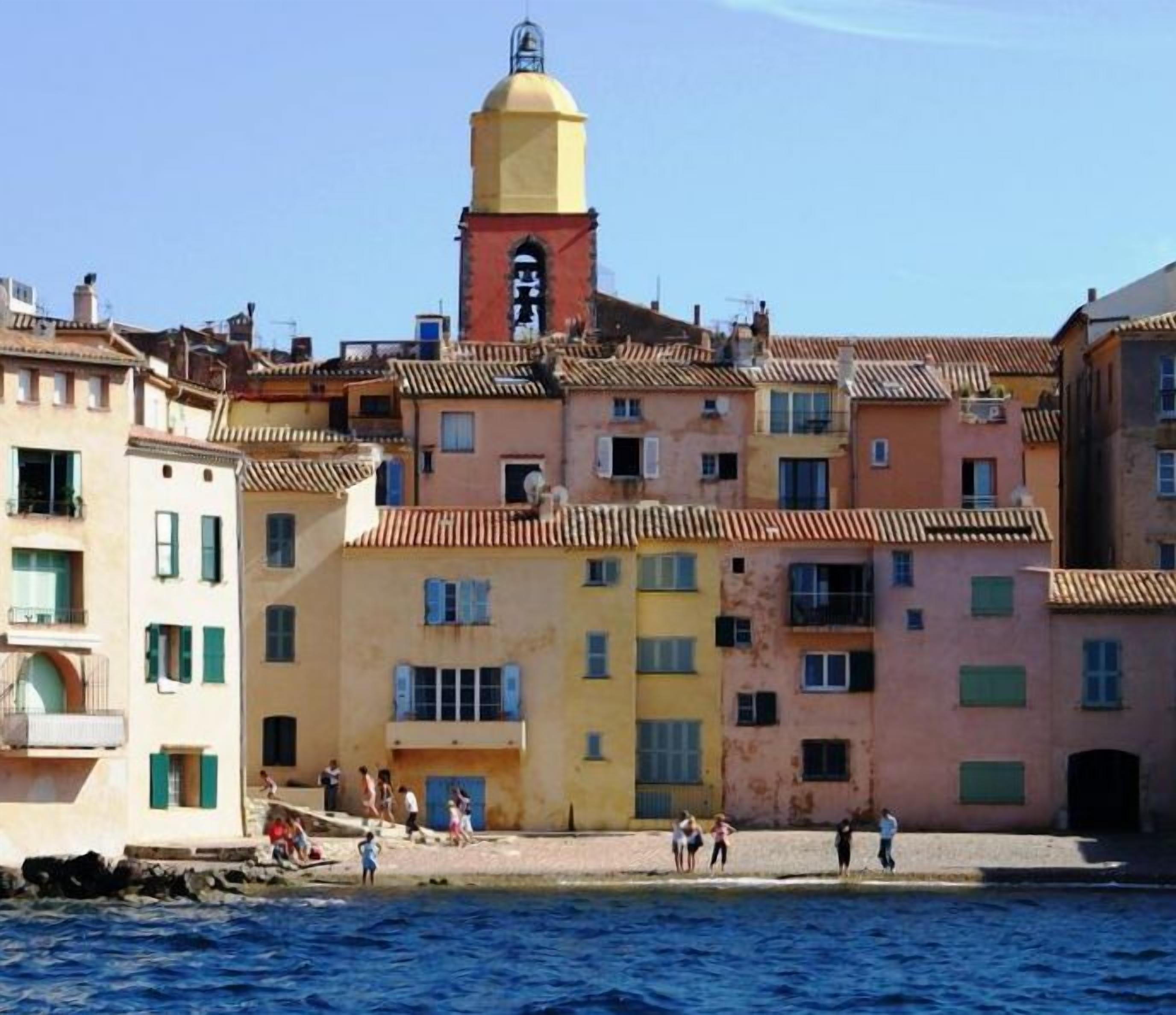 A coastal town with colorful buildings, a prominent yellow tower, and a clear blue sky.