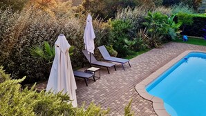 A pool area with lounge chairs and umbrellas, surrounded by lush greenery and a view of the sunset. - La Bastide, apartment with private pool near the Gulf of St Tropez (Fréjus)