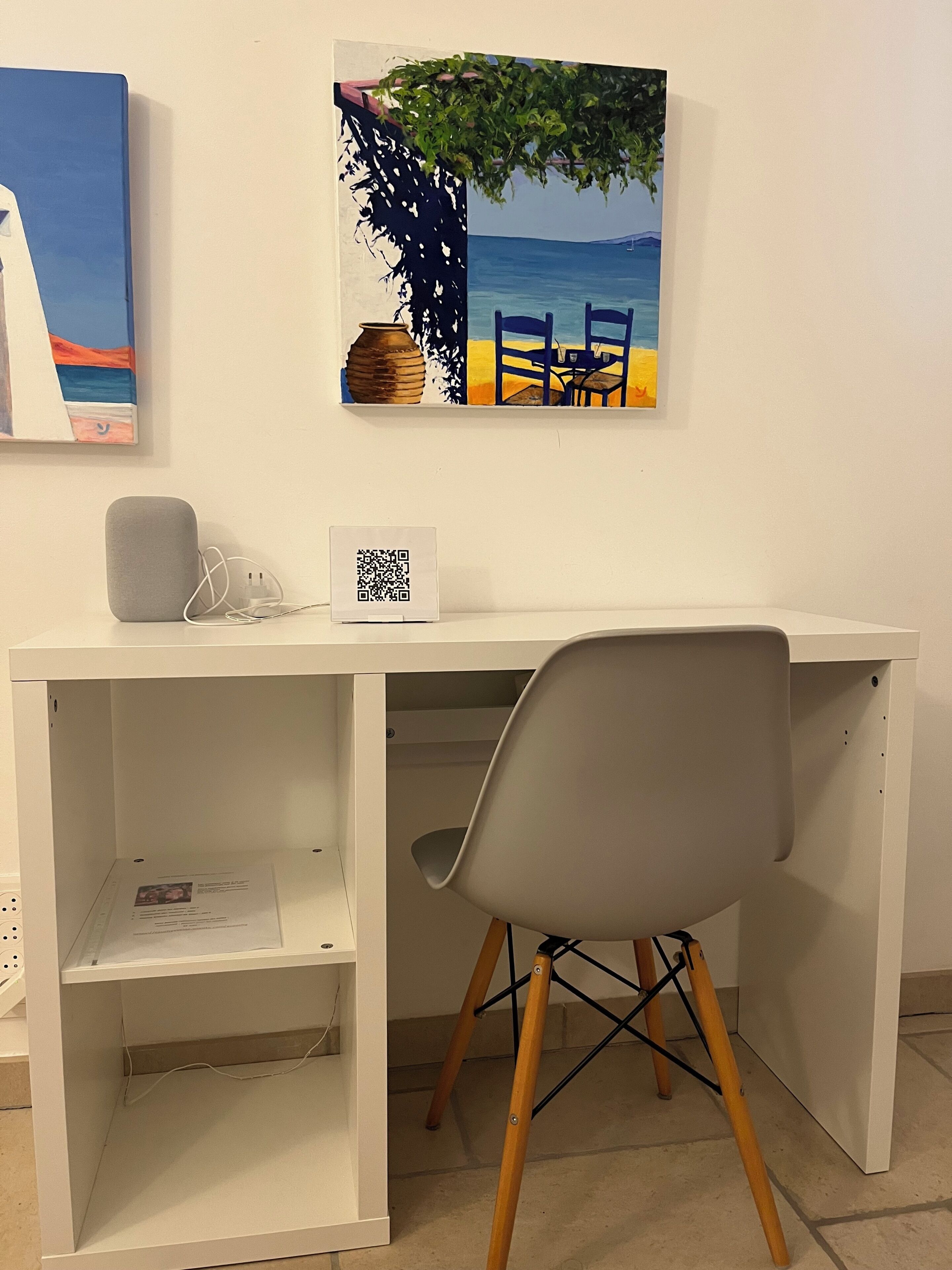 A white desk with a grey chair, a vase, and a QR code sign.