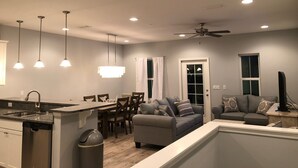 Una cocina moderna con lavavajillas incorporado, una zona de comedor con mesa y sillas, un sofá gris y un ventilador de techo.