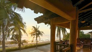 Un espacio de estar techado al aire libre con vista a la playa y palmeras.