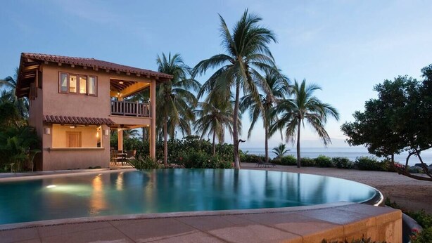 Una casa de dos pisos con balcón, piscina y palmeras.