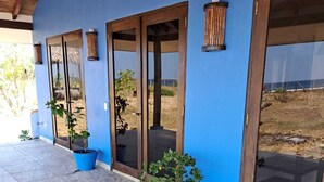 A building with blue walls and large glass doors, potted plants, and a tiled patio. - Surf, Sun & Serenity – 2BR Beachfront Home at Playa Tesoro (Between Salinas Grandes and Puerto Sandino)