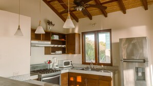 A modern kitchen with wooden cabinets, a stainless steel refrigerator, a microwave, a stove, and pendant lights. - Surf, Sun & Serenity – 2BR Beachfront Home at Playa Tesoro (Between Salinas Grandes and Puerto Sandino)