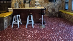 A bar area with a stone wall, a TV mounted on the wall, and a red speckled floor.