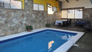 An indoor swimming pool with a stone wall, a table with chairs, and a hanging light fixture.