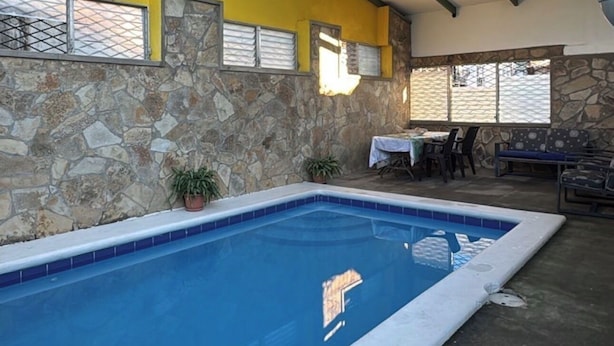 Una piscina interior con pared de piedra, una mesa con sillas y una lámpara colgante.