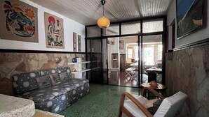 Una sala de estar con un sofá estampado, una silla de madera, una mesa de piedra y obras de arte en las paredes.