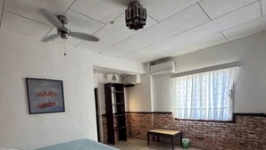 Un dormitorio con cama, ventilador de techo, ventana con cortinas y pared de ladrillo.