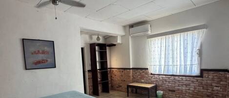 Un dormitorio con cama, ventilador de techo, ventana con cortinas y pared de ladrillo.
