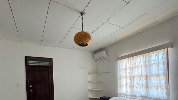 A bedroom with a bed, a desk, a door, and a hanging light fixture.