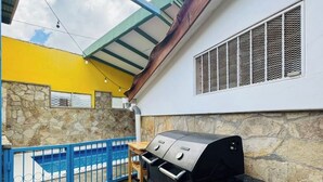 A barbecue grill in an outdoor patio area with a stone floor, a blue gate, and a yellow wall.