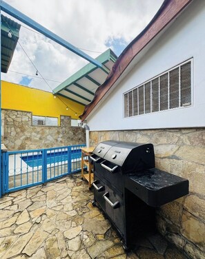 Una parrilla para barbacoa en un patio al aire libre con suelo de piedra, un portón azul y una pared amarilla.