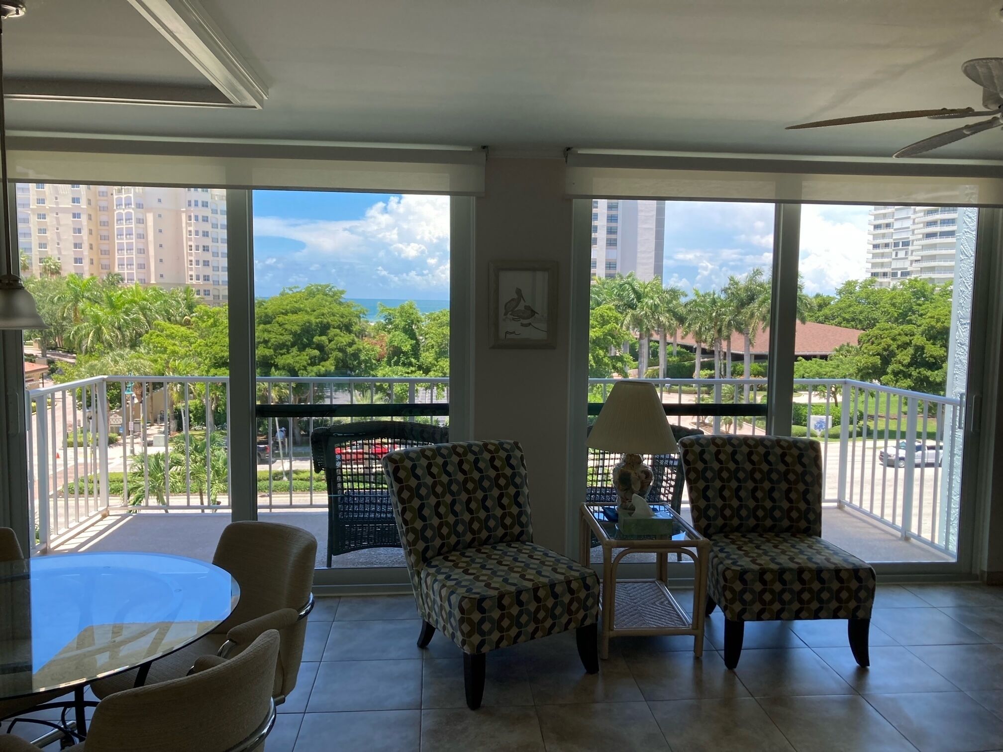 A balcony with two patterned chairs, a glass table, and a lamp.
