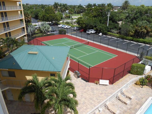 A multi-level building with a tennis court, a parking area, and a poolside area with seating. - Short term rentals, Beach access directly across the street (Marco Island)