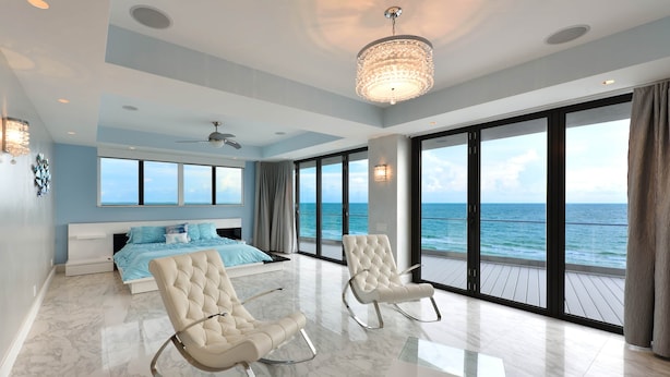 A modern bedroom with a large bed, two rocking chairs, a glass coffee table, and a view of the ocean. - Pure luxury at #Sunset Wave on the Beach (Treasure Island)