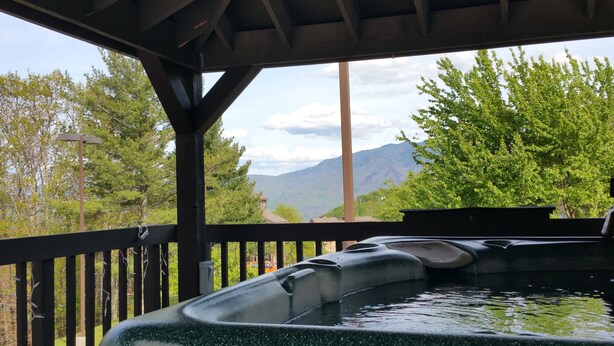 A hot tub under a wooden deck with a view of mountains and trees. - Gorgeous fall colors views from  mtn top condo! King bed hot tubs sauna. Promos! (Gatlinburg)