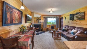 A cozy cabin interior with a dining area, a fireplace, a leather sofa, and large paintings on the walls. - Gorgeous fall colors views from  mtn top condo! King bed hot tubs sauna. Promos! (Gatlinburg)