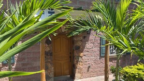 Ein Steinhaus mit Holztür, einer Backsteinmauer und einem kleinen Garten mit Palmen.