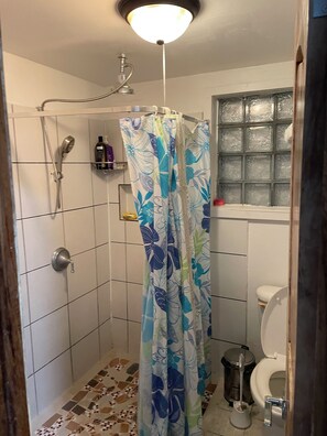 Un baño pequeño con azulejos, ducha, inodoro y ventana con vidrio esmerilado.