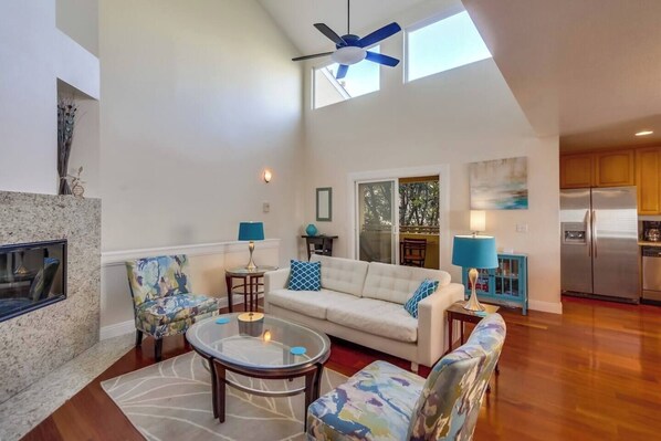A spacious living room with a high ceiling, a sofa, a coffee table, and a television.