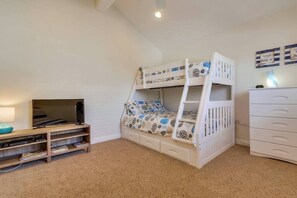 Ein Kinderstockbett mit gemusterten Bettbezügen, ein Fernseher auf einem Holzständer und eine weiße Kommode mit Schubladen.