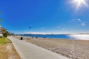 A beach with a concrete walkway, a clear sky, and a calm sea.