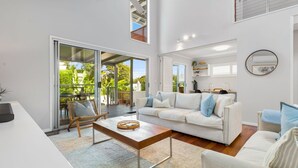 Un salon spacieux avec un canapé blanc, une table basse en bois et une porte-fenêtre coulissante donnant sur un espace extérieur.