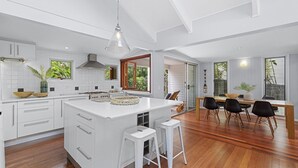 Une cuisine moderne avec des meubles blancs, un îlot central et un coin repas doté d’un plancher en bois et de chaises noires.
