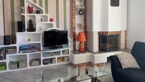 A living room with a TV on a glass shelf, a fireplace, and a sofa with a patterned pillow.