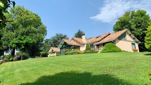 A two-story house with a tiled roof, surrounded by a well-maintained lawn and various plants.