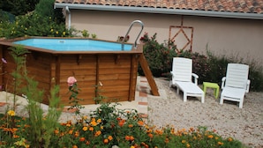 A backyard with a wooden swimming pool, two white lounge chairs, and a small green table.