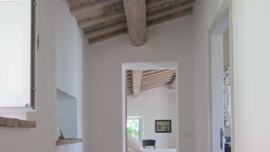 Ein schmaler Flur mit Backsteinboden, der zu einem Schlafzimmer mit Bett und Sessel führt.